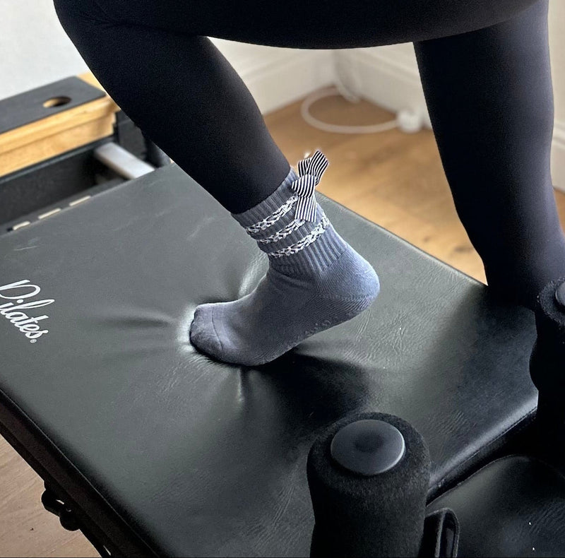 Gray grip socks with bows standing on a Pilates reformer carriage