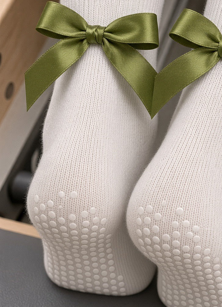 Close-up of white Pilates grip socks with green satin bows and silicone grip soles