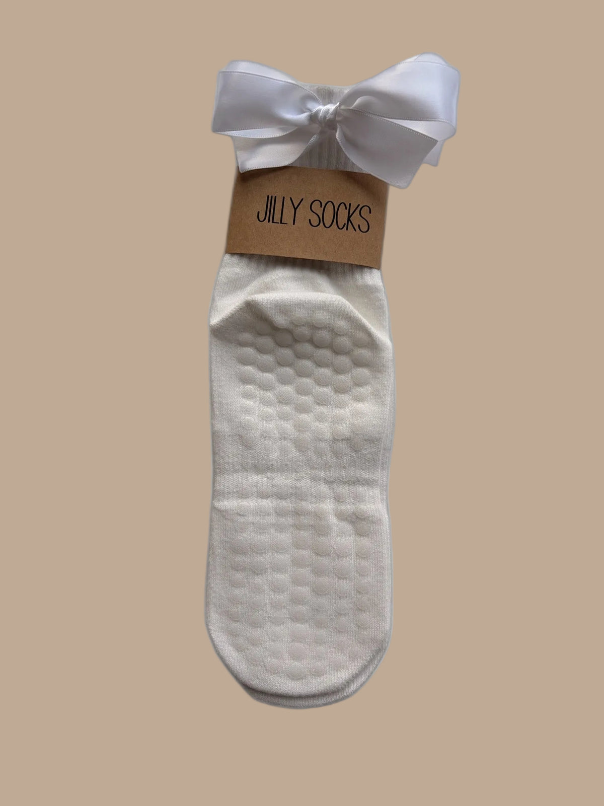 Cute, fashionable white Pilates grip socks with a white satin bow and a tan paper band reading 'JILLY SOCKS' on a white background.