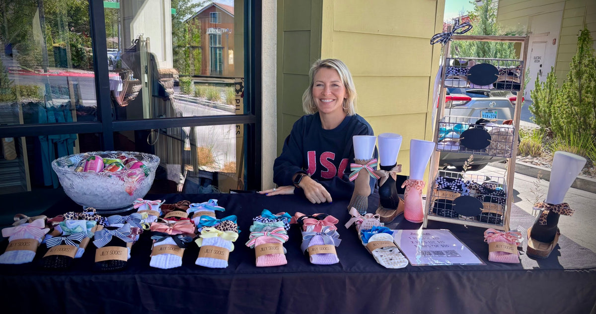 Jill at her Jilly Socks pop-up table outside a Pilates studio, with bow socks laid out in rows